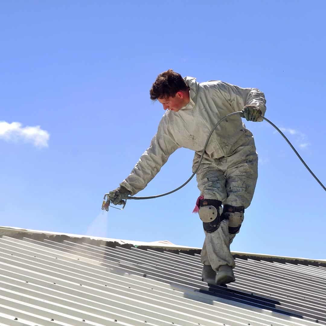 roofer spraying coating on a metal roof